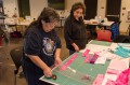 Thumbnail image of Ella Louise Weaver lends her expertise to another tribal member. During the first phase of quilt making, participants choose colors and work from intricate patterns to lay out their projects.