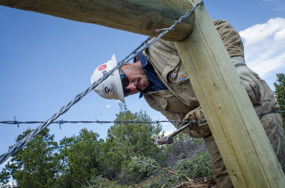 An employee of Crossfire LLC works to put the finishing touches on a robust section of fenceline near Alamo Canyon.