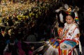 Thumbnail image of A young dancer gathers his regalia high above the grand entry taking place on the arena floor.