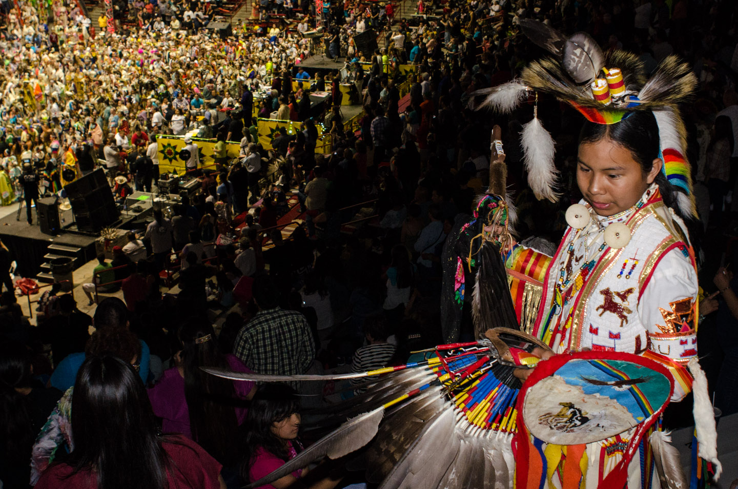 A young dancer gathers his regalia high above the grand entry taking place on the arena floor.