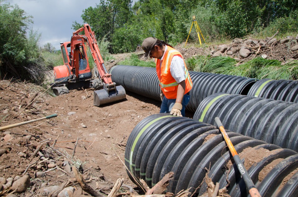 Herman Begay, irrigation supervisor for the U.S. Bureau of Indian Affairs, works with Soil Conservation Technician Preston Abeyta to fit parallel sections of plastic ADS culvert together, spanning a total of 120 feet through the damaged watercourse.