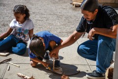 Participants learned how to make fire using traditional methods. Staff member, Tallas Cantsee helps his son try to make fire using a bow Tuesday, Aug. 5 at the Southern Ute Cultural Center and Museum. 