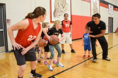 Trae Siebel (far right) assists the Lady Bobcat team as he coaches young participants through a lay-up drill. 