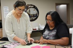 Lorna House pays close attention to Elise Redd while she teaches House how to quilt the pieces of the bear paw together.
