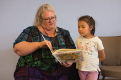Southern Ute Indian Montessori Academy teacher, Danielle Burns reads aloud to the attentive Sibrya Larry during the children’s book event held at Southern Ute Multi-Purpose Facility, Tuesday, May, 22.