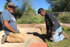 Grounds maintenance clean-up crew members, Jose Lucero and Ross Jacket install new stone tiles into the play area of the Southern Ute Indian Montessori Academy play area. 
