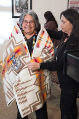 Southern Ute Chairman, Christine Sage wraps outgoing Councilwoman, Pearl Casias in a Pendleton blanket as a token of gratitude, during a farewell ceremony held in the Leonard C. Burch building, Friday, Nov. 30. 