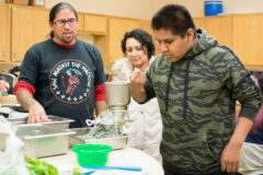 Chef Karlos Baca watches as Gunner Coyote grinds handfuls of blue corn, so the Cooking Matters class could make fresh pressed tortillas for their quesadillas and salsa. Baca led the class with the help of Shining Mountain Health and Wellness staff on Wednesday, Nov.13 in the kitchen of the Education Department. 