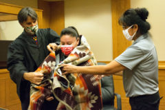 Judge Scott Moore and Senior Probation Officer Vanessa Torres wrap Jasmine Weaver in a Pendleton blanket in celebration of completing her time in the tuuCai Wellness Court on Thursday, Sep. 10 in the Southern Ute Tribal Courtroom. 
