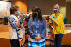Current  Tribal  Councilwomen,  Ramona  Eagle  and  Linda  Baker  wrap  Vanessa  Torres  in  a  Pendleton  blanket  on  Friday,  Dec.  3,  Tribal  Council  Affairs  hosted  the  End-of-Term  Celebration for both outgoing Vice Chairman Bruce Valdez and Council Member Torres.