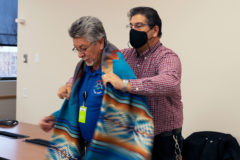 Southern Ute tribal employee, Fred Romero is wrapped in a Pendleton blanket by Custodial Services Supervisor, Jess Baidwan on Tuesday, Dec. 28 during a small reception at the Buckskin Charley Conference Room. Staff members from the Southern Ute Tribe’s Clean Team gathered in celebration of Fred Romero and his retirement from the Property and Facilities Management department. Romero has been with the Clean Team for 12 years.    