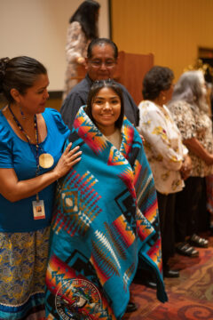 Southern Ute tribal member Angela Baker, a recent Ignacio High School graduate, is honored with a brand-new Pendleton blanket embroidered with the Southern Ute Tribal Seal and her name, Friday, June 24 at the 21st Annual Recognition hosted by the Southern Ute Education Department in the Sky Ute Casino Resort Event Center. Council Member Stacey Oberly draped the Pendleton over Baker’s shoulders and gave a brief congratulations on her educational accomplishments.  