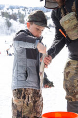 Jaxx Pena and his father Alex Pena take a trout he caught to weigh in at the Lake Capote Store during the Ice Fishing Tournament.  