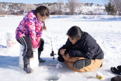 Ice fishing on Scott’s Pond — Clementine Carrillo and Aeden Richards visit with each other under clear blue skies, as they patiently watch the line — hoping for a fish to bite.  