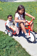 Lower Elementary student, O’Hozhoni Larry, gives Toddler student, Sylas Herrera, a ride on a toddler bicycle as part of a weekly classroom leadership activity.