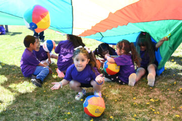 Primary three students enjoy the shade as teachers and family lift the parachute over the students.
