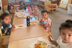 SUIMA Toddler 3 students are enjoying their first day of school snack.  Seen here are Tavach Litz, Chrissy Cloud, Nathan Ruybal, Nora’Lyn Goodtracks, Violet Powell, Scarlett Velasquez-Rodriquez, and Arnulfo Pardo IV; their teaching guides are Marilyn Olguin and Amanda Cray.