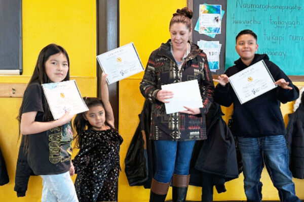 Alessa Herrera, Jinora Mills, and Meskvlwv Wesley receive certificates from SUIMA School Board President Rhiannon Velasquez for their participation in the school’s talent show.